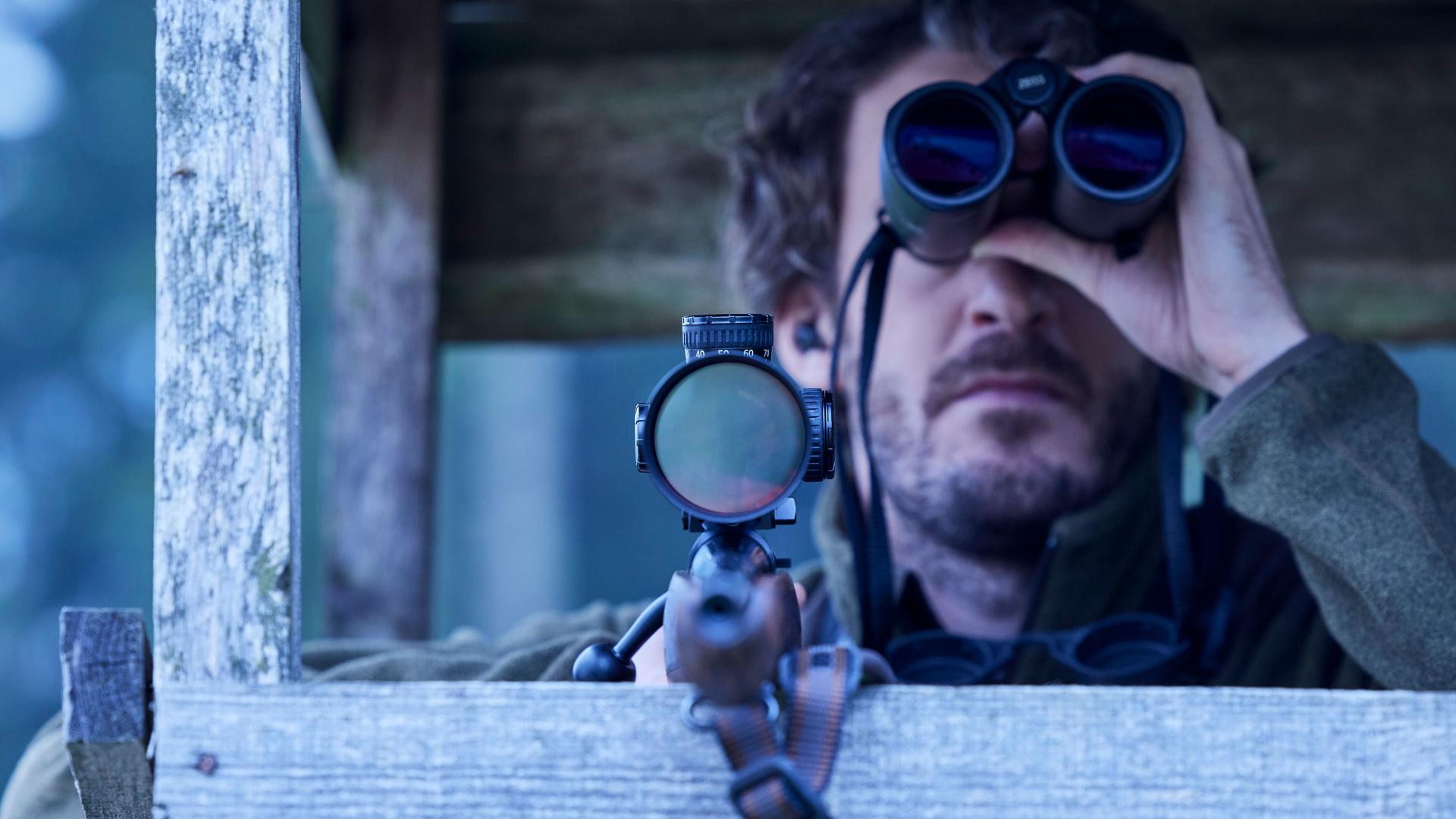 Hunter aiming through a ZEISS riflescope from a hide, showcasing the world’s finest illuminated dot for pinpoint accuracy.