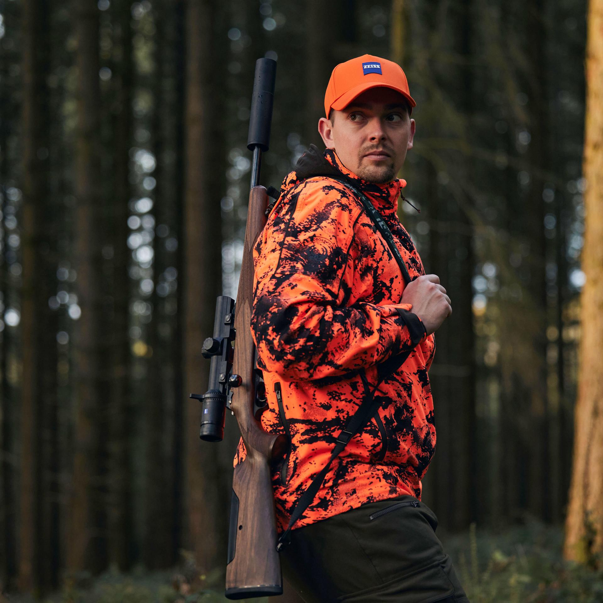 Hunter in an orange camouflage jacket carrying a rifle with a ZEISS Conquest V6 1.1–6x24 riflescope, ideal for fast target acquisition during driven hunts.