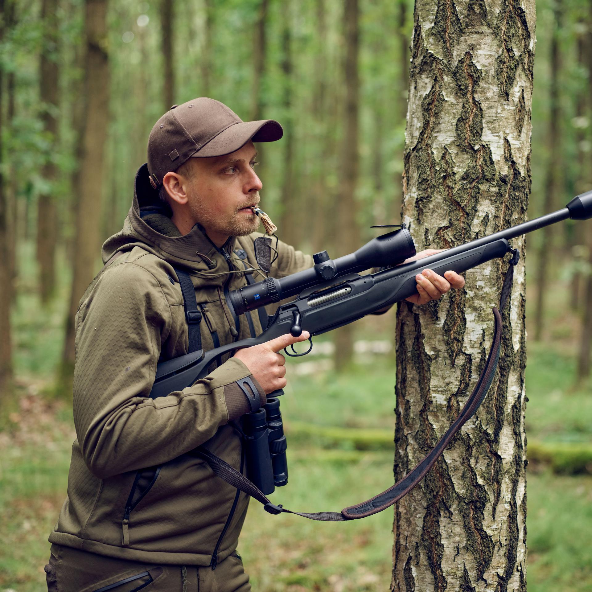 Hunter in a forest aiming with a rifle equipped with a ZEISS Conquest V6 2–12x50 riflescope, designed for versatile all-day hunting.