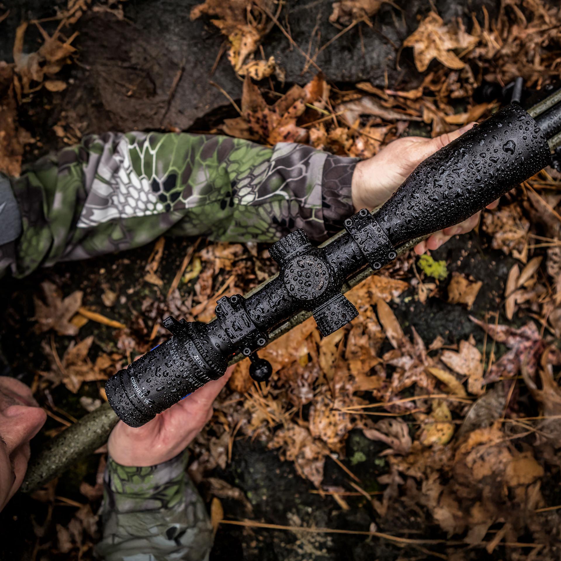 Close-up of a hunter holding a rifle with a ZEISS Conquest V6 5–30x50 riflescope covered in raindrops, built for long-range precision in tough weather conditions.