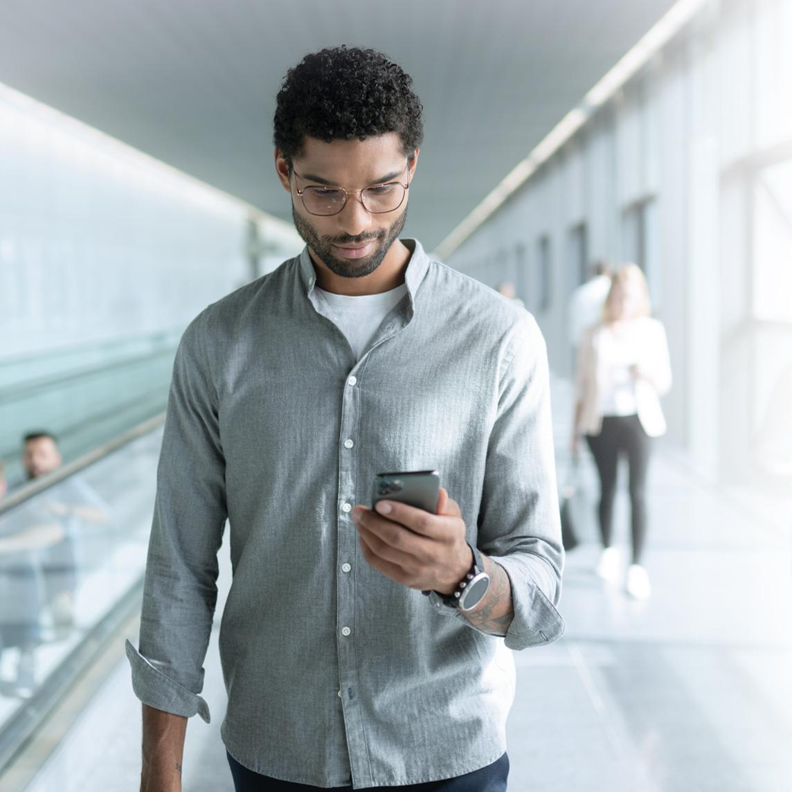 歩きながらスマートフォンを見る、ZEISS SmartLifeレンズを着けた若い男性。