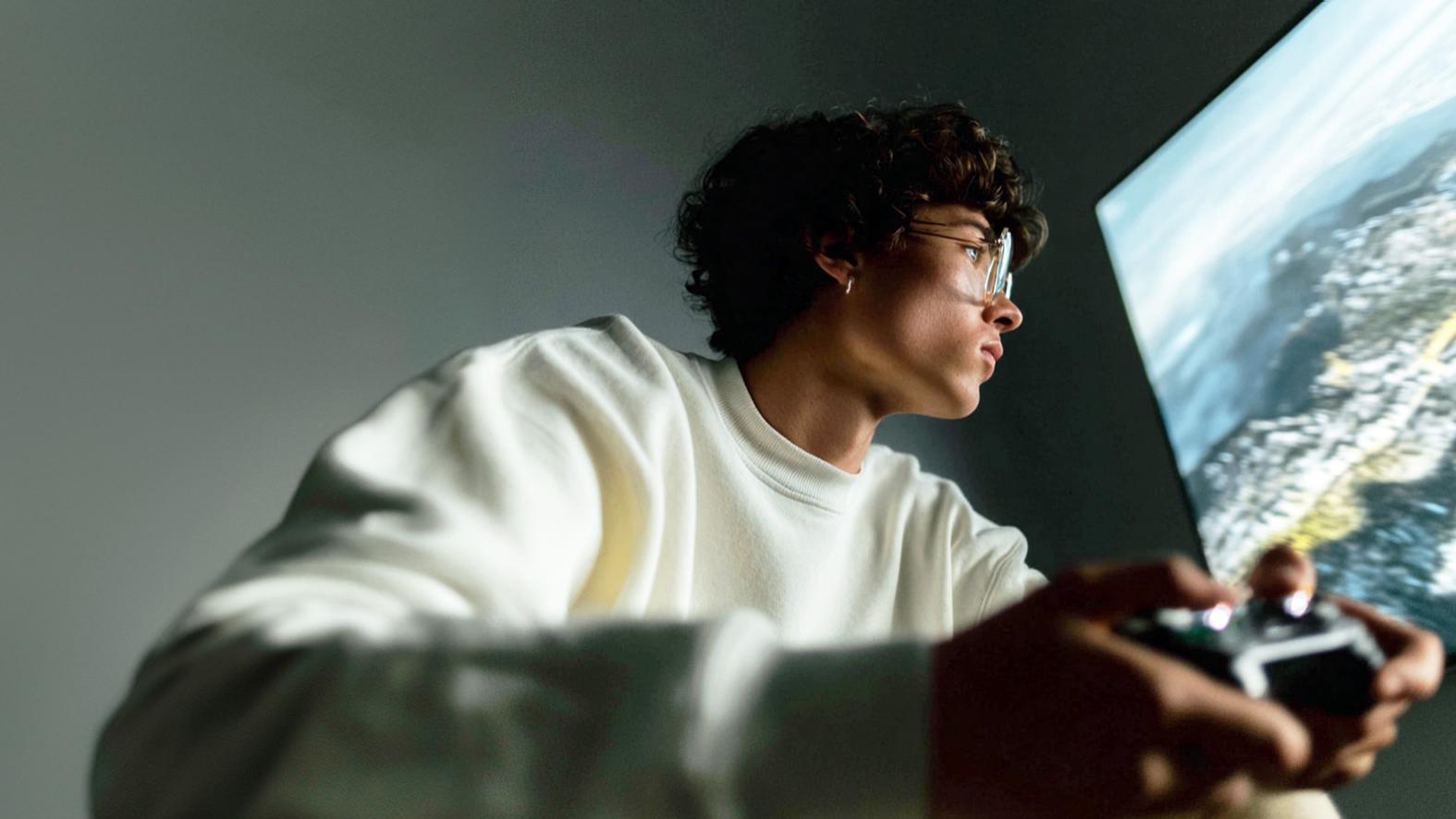 A young man wearing eyeglasses while playing a video game on a big screen