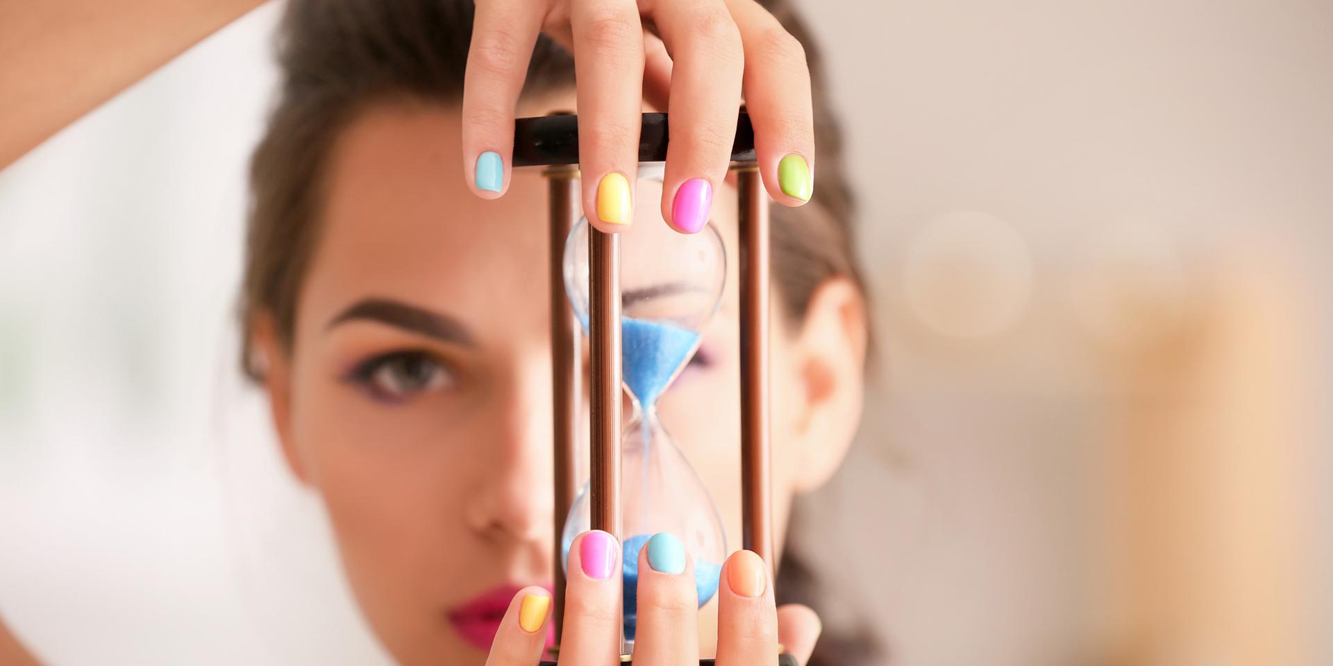 Young woman with colorful manicure holding hourglass