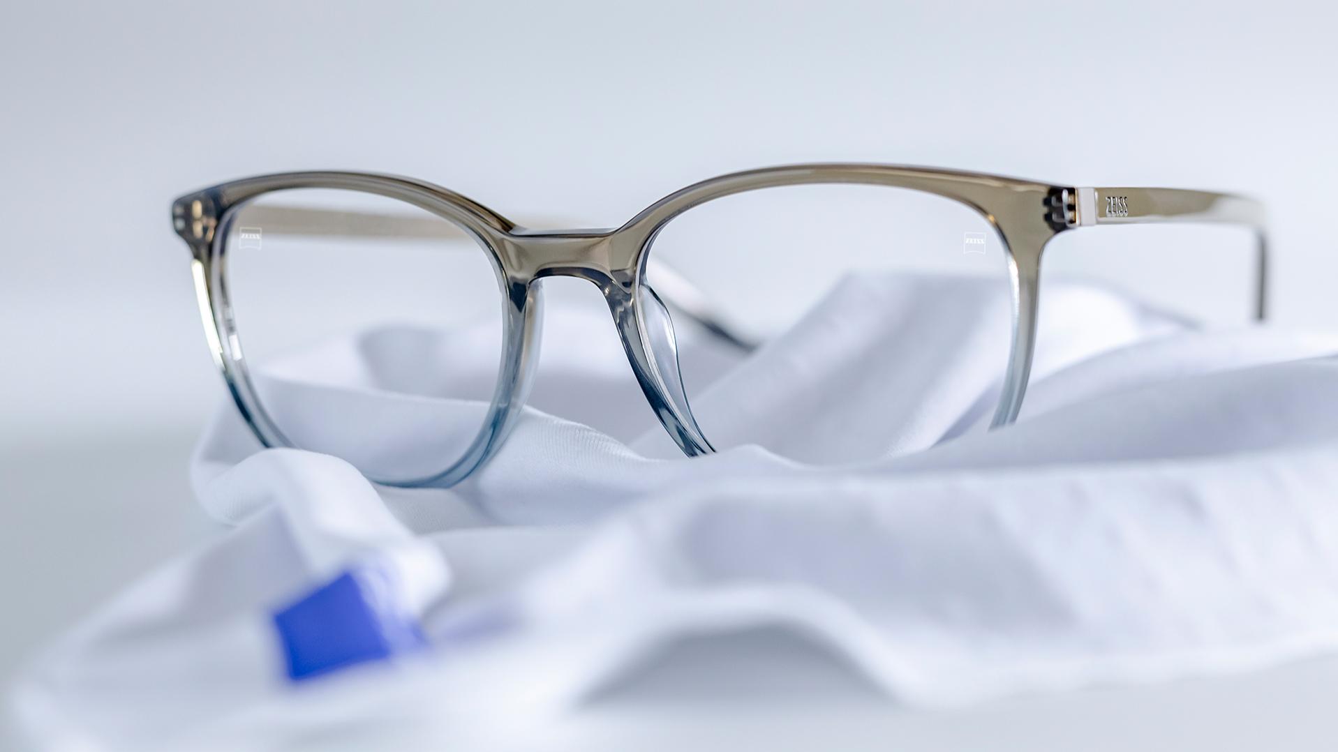 ブルーグレーのフレームとZEISS DuraVision®コーティングレンズのメガネが白いマイクロファイバークロスの上に置かれている。