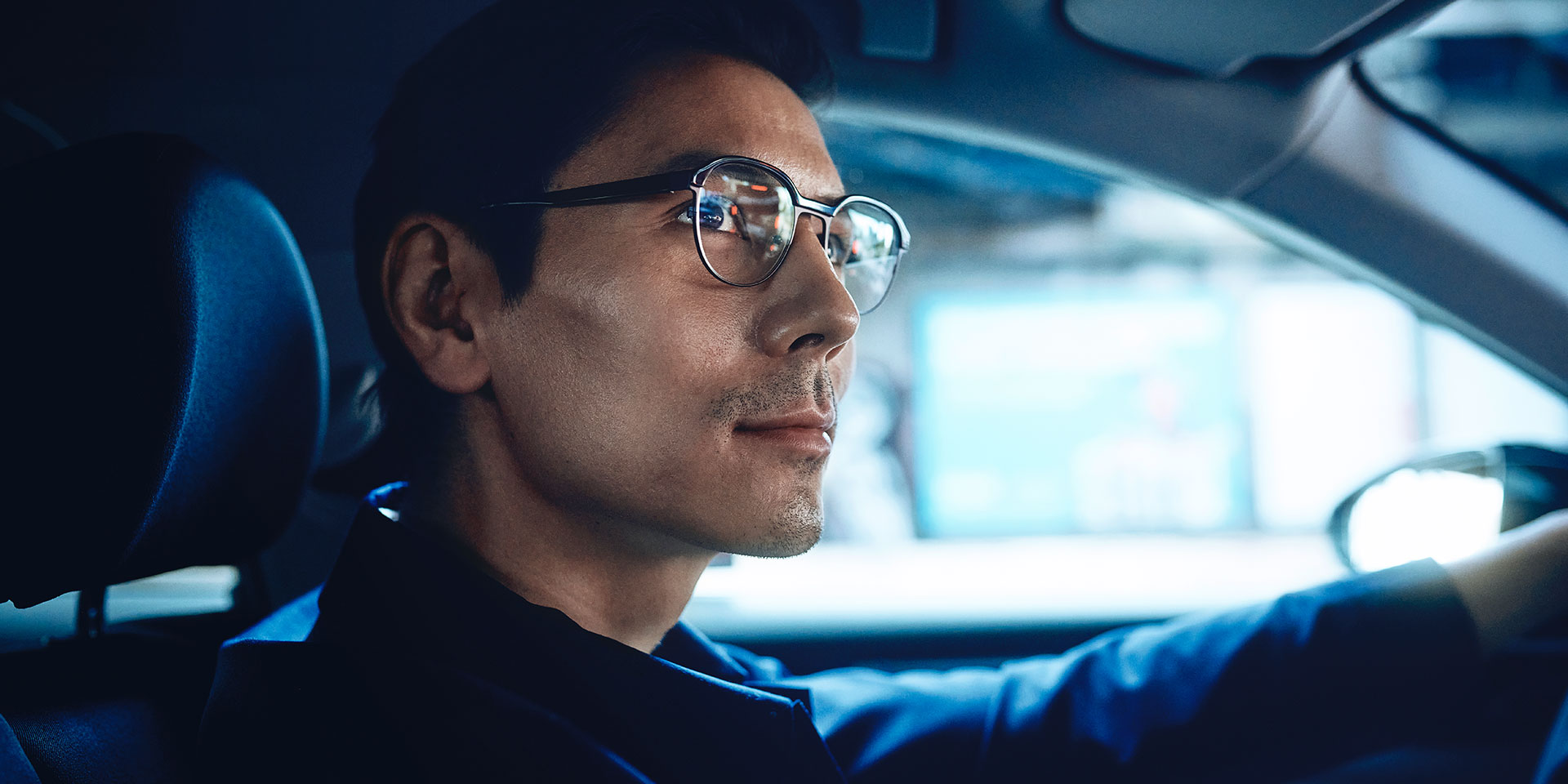 微笑んで、自信ありげに運転する男性。彼はZEISS DriveSafe単焦点レンズを掛けている。