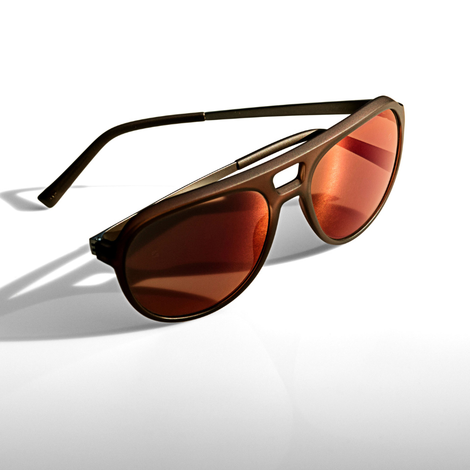 Sunglasses with an orange mirror effect on a white surface and light shining from the side.