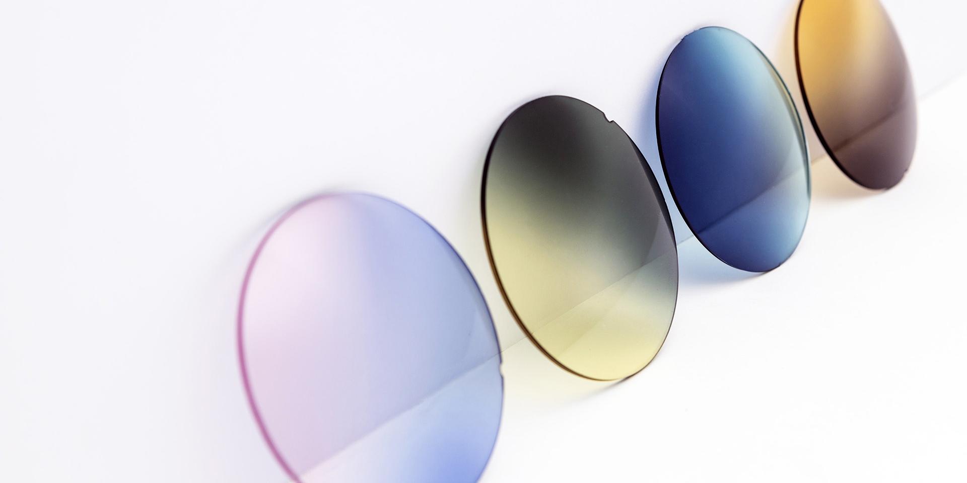 白い壁に立てかけた色とりどりのサングラス　レンズ（ピンクパープル、イエローグレー、ブルーおよびブラウンのグラデーション）。