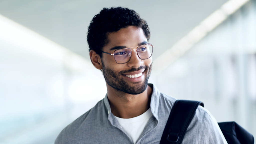 肩にバックパックをかけ、笑顔を見せる、ZEISS Digital SmartLifeレンズを装用し横を向いている若い男性。